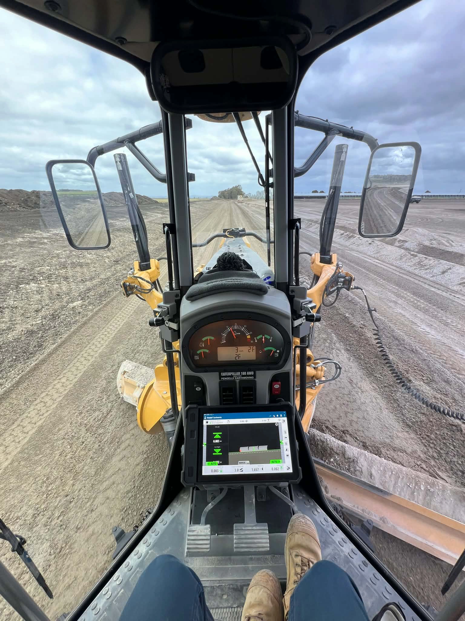 Inside the cab of Pengelly Cat 160M AWD grader — Trimble Earthworks display showing live grade control data on a Melbourne job site